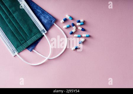 Mehrere Pillen und orale Kapseln auf einer medizinischen Einweg-Gesichtsmaske vor rosa Hintergrund. Stockfoto