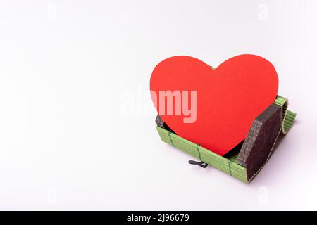 Papierrotes Herz in einer offenen grünen kleinen, Weidenbrust, Behälter auf einem hellrosa Hintergrund. Valentinskarte zum Valentinstag. Designelement. Stockfoto