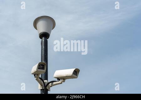 Überwachungskameras auf einem Lampenpfosten gegen einen blauen Himmel montiert. Sicherheits-cctv-Kamera. Sicherheit in der Stadt. Versteckte Dreharbeiten von dem, was passiert. Modder Stockfoto