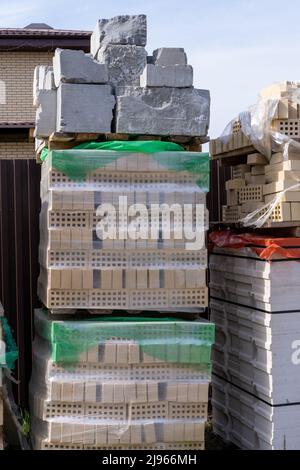 Hausbau. Betonblöcke und braune Ziegel für den Bau eines Hauses in mehreren Reihen auf Holzpaletten, vertikaler Rahmen gestapelt. Das Gebäude mater Stockfoto