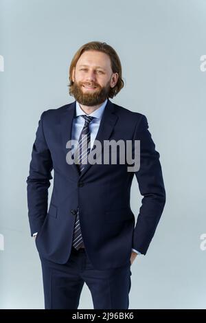 Ein hübscher, brutaler bärtiger und langhaariger Mann, ein stilvoller Geschäftsmann auf weißem Hintergrund Stockfoto