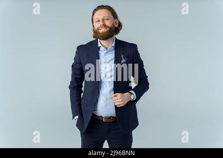 Ein hübscher, brutaler bärtiger und langhaariger Mann, ein stilvoller Geschäftsmann auf weißem Hintergrund Stockfoto