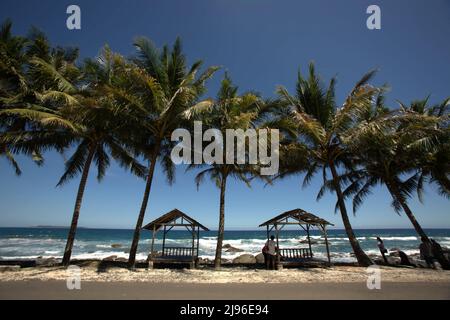 Erholsame Holzhütten unter Kokospalmen an einem Strand mit Blick auf den Indischen Ozean in Kotakarang, Pesisir Barat, Lampung, Indonesien. Stockfoto