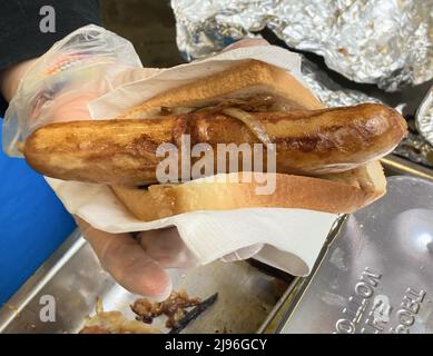 Sydney, Australien. 21.. Mai 2022. Ein Wahlhelfer bietet vor einem Wahllokal der Fort Street Public School in Sydney, Australien, eine gebratene Wurst in Toast an. Eine Besonderheit der australischen Wahlen sind die sogenannten Demokratiewürste. Traditionell gibt es vor vielen Wahllokalen einen Grill, wo die Wähler eine Art Hotdog essen können (Knockwurst in einem weichen Brötchen mit Senf und Ketchup). Mittlerweile gibt es auch vegetarische Alternativen und steht mit Kaffee und Kuchen. Quelle: Carola Frentzen/dpa/Alamy Live News Stockfoto