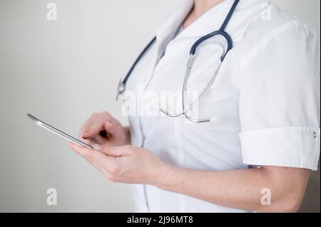 Nicht erkennbare Ärztin benutzt Handy. Der Arzt kommuniziert mit den Patienten über ein Smartphone. Abgeschnitten. Stockfoto