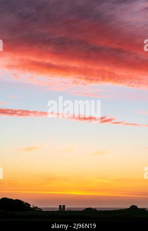 Der Morgenhimmel über der Nordsee in der Ferne mit der Landschaft von Kent im Vordergrund. Gerstenfeld und verstreute Baumgruppen, die sich am Horizont und am Meer abheben. Der Himmel ist am Horizont klar, eine dicke Schicht rötlicher Wolken darüber. Stockfoto