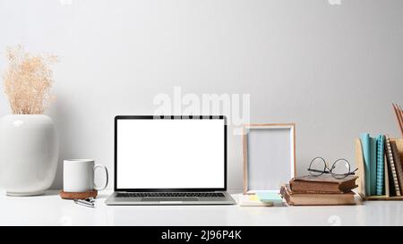 Komfortabler Arbeitsplatz mit Laptop-Computer, Bilderrahmen, Blumentopf, Kaffeetasse und Papeterie auf weißem Tisch Stockfoto