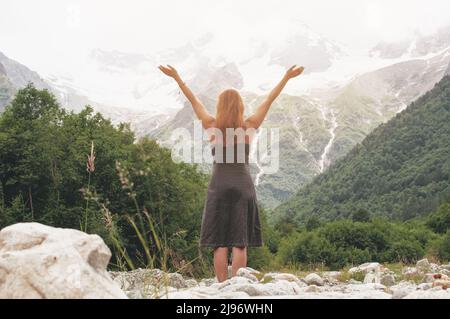 Rückseite der kaukasischen rothaarigen Frau, die im Sommer in den Bergen die Hände hochhebt und Glück und Freiheit fühlt. Bucket-Liste Stockfoto