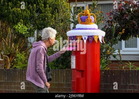 Weymouth, Dorset, Großbritannien. 21. Mai 2022. Ein Bewohner postet einen Brief an einer Briefbox in Weymouth in Dorset, die mit einer gehäkelten Staatskrone zur Feier des Platin-Jubiläums der Königin geschmückt wurde. Das Platin-Jubiläum von Elisabeth II. Wird vom 2. Juni bis 5. Juni 2022 im Vereinigten Königreich und im Commonwealth zum 70.. Jahrestag des Beitritts von Königin Elizabeth II. Am 6. Februar 1952 gefeiert. Bildnachweis: Graham Hunt/Alamy Live News Stockfoto