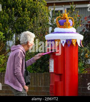 Weymouth, Dorset, Großbritannien. 21. Mai 2022. Ein Bewohner postet einen Brief an einer Briefbox in Weymouth in Dorset, die mit einer gehäkelten Staatskrone zur Feier des Platin-Jubiläums der Königin geschmückt wurde. Das Platin-Jubiläum von Elisabeth II. Wird vom 2. Juni bis 5. Juni 2022 im Vereinigten Königreich und im Commonwealth zum 70.. Jahrestag des Beitritts von Königin Elizabeth II. Am 6. Februar 1952 gefeiert. Bildnachweis: Graham Hunt/Alamy Live News Stockfoto