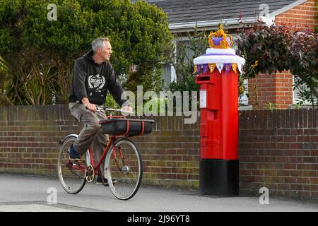 Weymouth, Dorset, Großbritannien. 21. Mai 2022. Ein Radfahrer passiert eine Briefbox in Weymouth in Dorset, die mit einer gehäkelten Staatskrone zur Feier des Platin-Jubiläums der Königin geschmückt wurde. Das Platin-Jubiläum von Elisabeth II. Wird vom 2. Juni bis 5. Juni 2022 im Vereinigten Königreich und im Commonwealth zum 70.. Jahrestag des Beitritts von Königin Elizabeth II. Am 6. Februar 1952 gefeiert. Bildnachweis: Graham Hunt/Alamy Live News Stockfoto