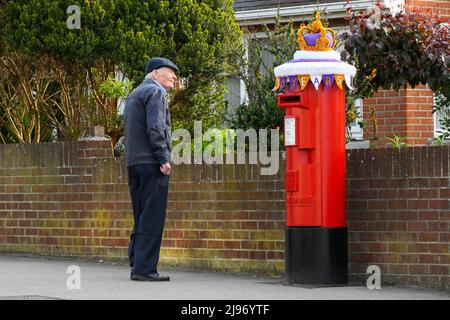 Weymouth, Dorset, Großbritannien. 21. Mai 2022. Ein Bewohner hält an, um sich eine Briefbox in Weymouth in Dorset anzusehen, die zur Feier des Platin-Jubiläums der Königin mit einer gehäkelten Staatskrone geschmückt wurde. Das Platin-Jubiläum von Elisabeth II. Wird vom 2. Juni bis 5. Juni 2022 im Vereinigten Königreich und im Commonwealth zum 70.. Jahrestag des Beitritts von Königin Elizabeth II. Am 6. Februar 1952 gefeiert. Bildnachweis: Graham Hunt/Alamy Live News Stockfoto