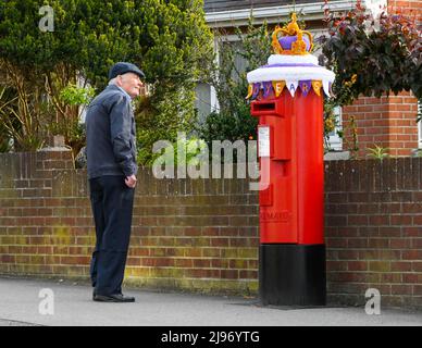 Weymouth, Dorset, Großbritannien. 21. Mai 2022. Ein Bewohner hält an, um sich eine Briefbox in Weymouth in Dorset anzusehen, die zur Feier des Platin-Jubiläums der Königin mit einer gehäkelten Staatskrone geschmückt wurde. Das Platin-Jubiläum von Elisabeth II. Wird vom 2. Juni bis 5. Juni 2022 im Vereinigten Königreich und im Commonwealth zum 70.. Jahrestag des Beitritts von Königin Elizabeth II. Am 6. Februar 1952 gefeiert. Bildnachweis: Graham Hunt/Alamy Live News Stockfoto