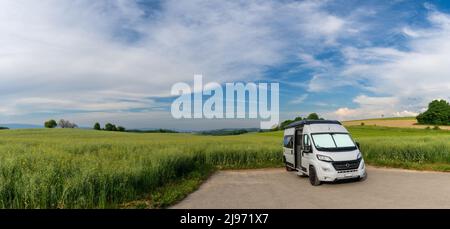 Panorama-Landschaft mit einem grauen Wohnmobil in einer idyllischen Landschaft mit Weizenfeldern und Wald geparkt Stockfoto