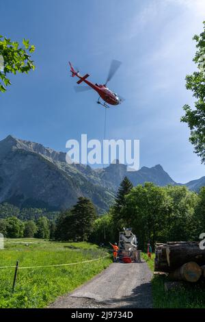 Maienfeld, Schweiz - 20. Mai 2022: Bauarbeiter verladen Ladung und Zementeimer zu einem Hubschrauber für einen alpinen Transport in den Schweizer Alpen Stockfoto