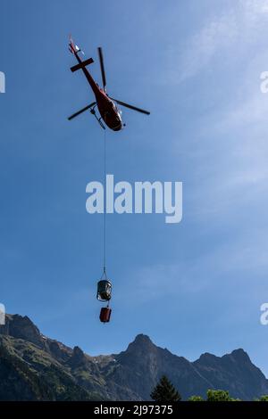 Maienfeld, Schweiz - 20. Mai 2022: Helikopter mit einem Eimer Zement zu einer entfernten Berghütte in den Schweizer Alpen Stockfoto