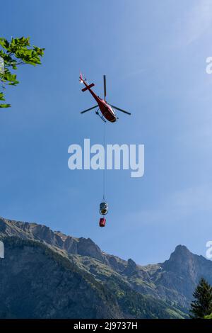 Maienfeld, Schweiz - 20. Mai 2022: Helikopter mit einem Eimer Zement zu einer entfernten Berghütte in den Schweizer Alpen Stockfoto