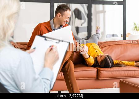 Hand eines professionellen Familien-Psychotherapeuten, der während einer Konsultation Notizen vor einer Familie mit einem Kind schreibt Stockfoto