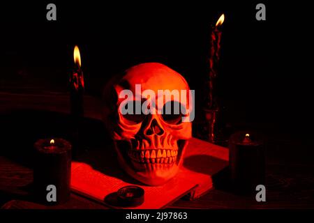 Der menschliche Schädel und Kerzen mit orangefarbenem Licht im Dunkeln. Gruselige gruselige Sachen für halloween oder satanisches Ritual. Stockfoto