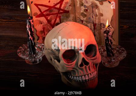 Nahaufnahme des Menschen Schädel mit Kerzen und bibel mit Pentagramm. Antichrist satanisches rituelles Konzept. Stockfoto