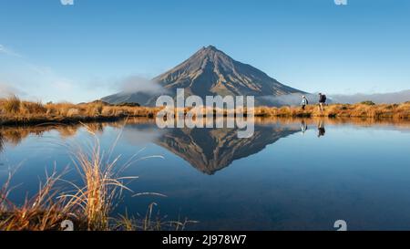 Zwei Personen wandern auf dem Pouakai-Rundkurs. Mt Taranaki spiegelte sich im tarn in der frühen Morgensonne wider Stockfoto