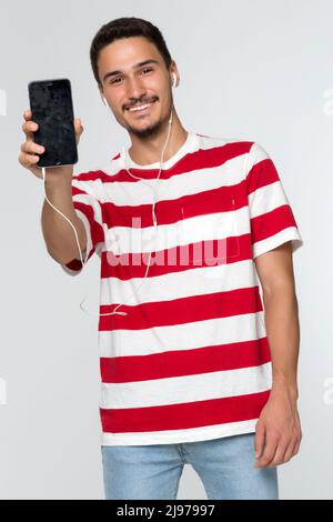 Unfokussierte junge Mann Hand zeigt Ihnen ein leeres Smartphone mit Kopfhörer in weißem Hintergrund. Stockfoto