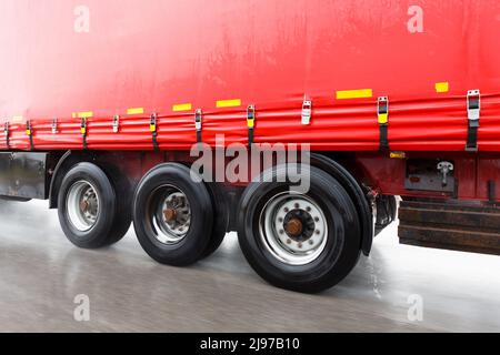 Ein roter LKW, der auf einer vom Regen nassen Straße mit Wasser rund um die Reifen fährt. Stockfoto