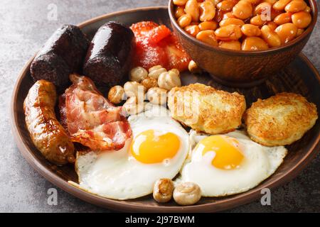 Komplettes irisches Frühstück, schwarzer Pudding, Eier, Bohnen, Würstchen, Speck, Hash braun, Tomate in der Nähe in der Platte auf dem Tisch. Horizontal Stockfoto