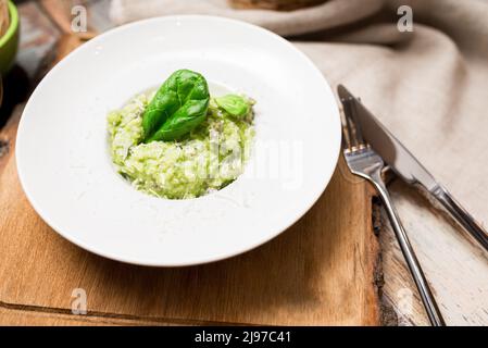 Servierplatte aus grünem Risotto mit Basilikumblättern und Käse. Gesunde Ernährung. Zartes arborio mit Spinatgemüse und mit Lammfleisch brot angereichert Stockfoto