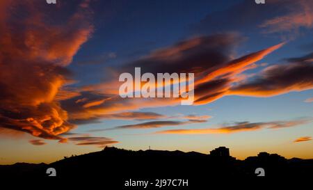 Wunderschöne orangefarbene Wolken am blauen Himmel mit silhouttigem Schattenhügel. Stockfoto