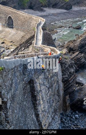 Bakio, Spanien - 3. Mai 2022: Seilzugänge und Bauarbeiter reparieren historische Steinmauern und Brücken an der Küste des spanischen Baskenlandes Stockfoto