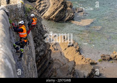 Bakio, Spanien - 3. Mai 2022: Seilzugänge und Bauarbeiter reparieren historische Steinmauern und Brücken an der Küste des spanischen Baskenlandes Stockfoto