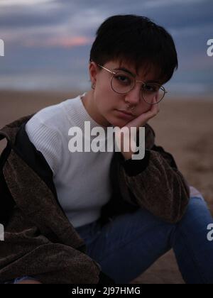 Müde transsexuelle Frau, die am Strand sitzt und ihren Kopf mit dem Arm hält Stockfoto