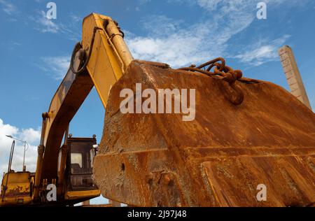 Nahaufnahme rostiger Metalleimer von alten Baggerlader, der auf der Baustelle vor blauem Himmel geparkt ist. Baggermaschine. Maschine mit Erdbewegung. Aushubfahrzeug. Stockfoto