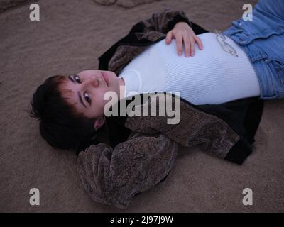 Transgender-Frau, die auf dem Sand liegt und ihren Kopf auf der Hand hält Stockfoto