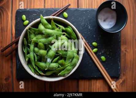 Gedämpftes Edamame, bestreut mit Meersalz auf einem dunklen Steinbrett, Draufsicht Stockfoto