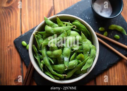 Gedämpftes Edamame, bestreut mit Meersalz auf einem dunklen Steinbrett, Draufsicht Stockfoto