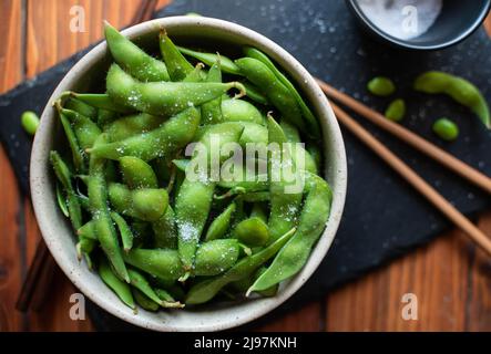 Gedämpftes Edamame, bestreut mit Meersalz auf einem dunklen Steinbrett, Draufsicht Stockfoto