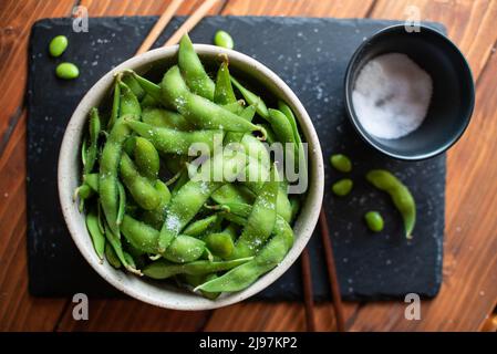 Gedämpftes Edamame, bestreut mit Meersalz auf einem dunklen Steinbrett, Draufsicht Stockfoto