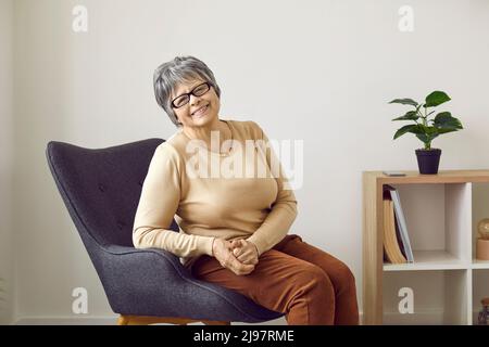Lächelnde reife Frau entspannen sich im Sessel Stockfoto