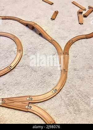 Kindereisenbahn aus Holz auf weißem, flauschigen Teppich. Kind spielte und baute Straße mit Gabeln. Mehrere Teile waren nicht nützlich und liegen in der Nähe. Stockfoto