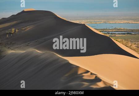 Sonnenuntergangslandschaft mit singenden Sanddünen barkhan und dem Fluss ili im berühmten Altyn Emel Nationalpark in der Nähe von Almaty, Kasachstan Stockfoto