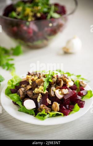 Salat mit gekochten Rüben, gebratenen Auberginen, Kräutern und Rucola auf dem Teller, auf dem Holztisch. Stockfoto