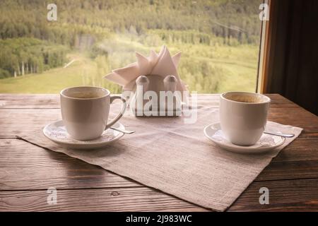 Zwei weiße Keramik-Kaffeetassen auf einem Holztisch. Panoramablick auf die Natur. Stockfoto