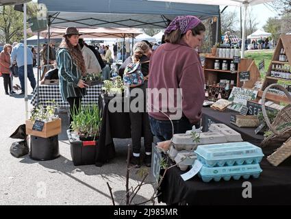 Eine Verkäuferin beobachtet, wie zwei Frauen die Waren während des Tower Grove Farmer's Market am 16. April 2022 in St. Louis, MO, USA, zum Verkauf durchsehen. Stockfoto