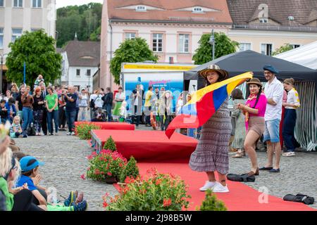 Ostritz, Deutschland. 21.. Mai 2022. Eine Frau tanzt mit einem Hut auf dem Kopf und hält die Flagge Ecuadors an der Modenschau, die das Thema Demokratie, Kosmopolitismus und Toleranz hat. Das Friedensfestival ist seit Jahren ein integraler Bestandteil der Gemeinschaft, um sich gegen rechtsorientierte Veranstaltungen in der Stadt zu wehren. Quelle: Daniel Schäfer/dpa/Alamy Live News Stockfoto