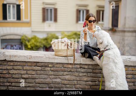 Frau, die Eis isst, während sie mit Hund auf einer Straße im Freien sitzt Stockfoto