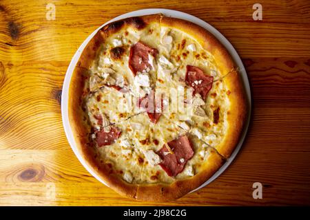 Pizza mit Sauce, Huhn, Käse auf dem Teller auf Holztisch serviert. Stockfoto