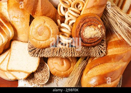Kulinarischer Hintergrund mit Brot, Brötchen, trocknenden Bagels, Weizenohren in einem Korbkorb, Draufsicht Stockfoto