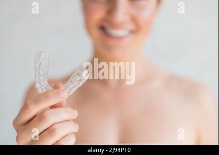 Nahaufnahme eines kieferorthopädischen Silikon-Transparent-Zahnausrichters in den weiblichen Händen. Verschwommene, nicht erkennbare Frau hält einen abnehmbaren Nachthalter. Halterung für Stockfoto